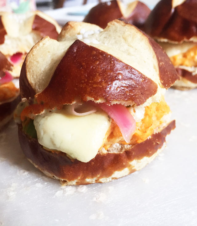 Buffalo chicken melt sliders, with blue cheese and pickled red onion on a pretzel slider.