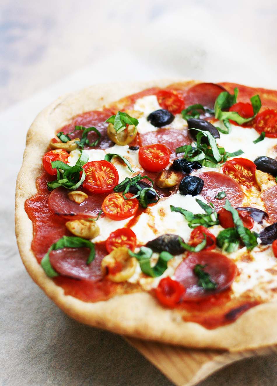 Charcuterie pizza, with tomatoes, salami, kalamata olives, fresh mozzarella, and basil chiffonade